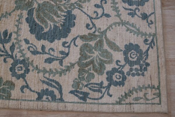 Beige rug featuring a dense floral pattern in blue-green and olive tones on light wood floor.