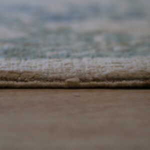 Thick cream pile rug edge and blurred blue pattern resting on smooth light brown flooring.