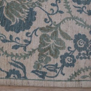 Beige rug featuring a dense floral pattern in blue-green and olive tones resting on light wood floors.