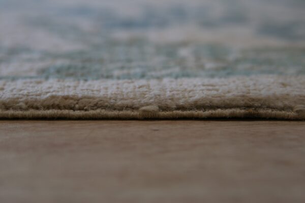 Side view of a cream and blue patterned rug with visible medium pile resting on wood flooring.