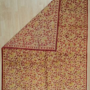 Beige and red floral rug partially folded back, revealing light wood plank flooring beneath.