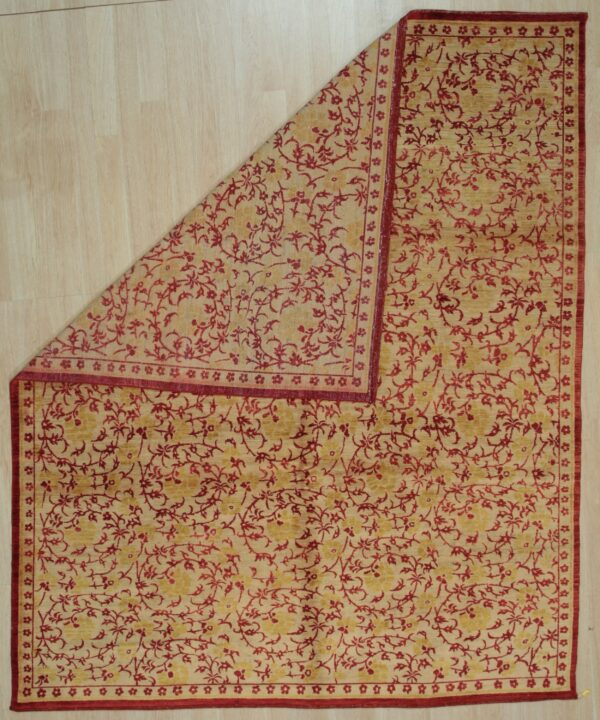 Beige and red floral rug partially folded back, revealing light wood plank flooring beneath.