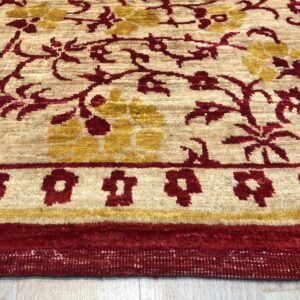 Textured cream rug with red and gold floral vine patterns and a strong red border on wood floor.