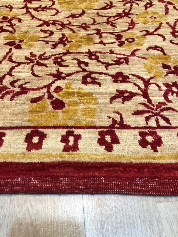 Textured cream rug with red and gold floral vine patterns and a strong red border on wood floor.