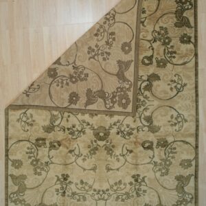 Beige and taupe floral rug lying on light wood flooring with one corner folded back diagonally.