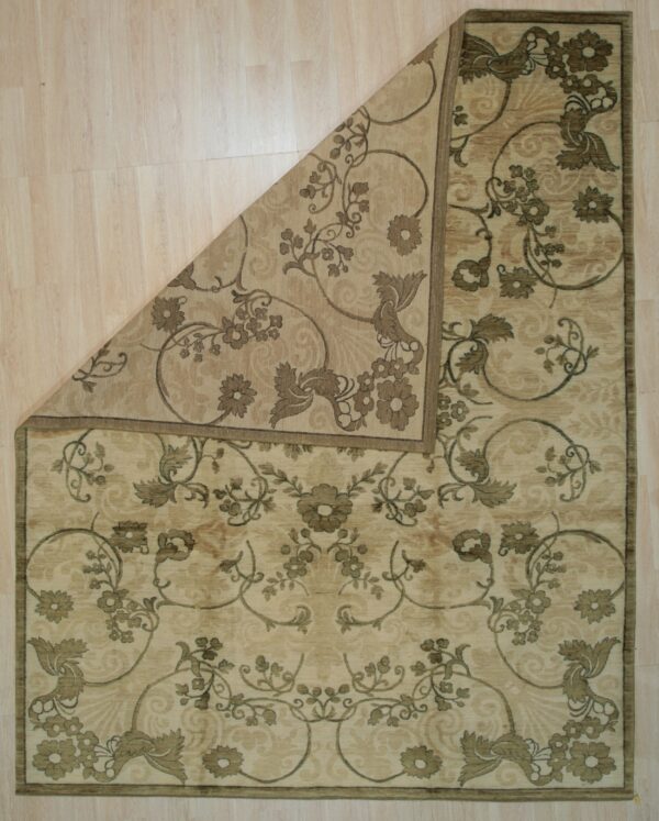 Beige and taupe floral rug lying on light wood flooring with one corner folded back diagonally.