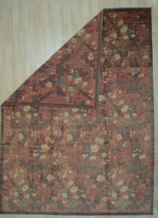 Rust-colored rug with dark scrolling floral patterns and cream flowers, partially folded on light wood floor.