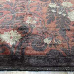 Ornate low pile rug in salmon pink, charcoal gray, and cream on light wood plank flooring.