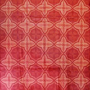 A plush crimson rug features a repeating trellis pattern of light pink stylized floral quatrefoils.