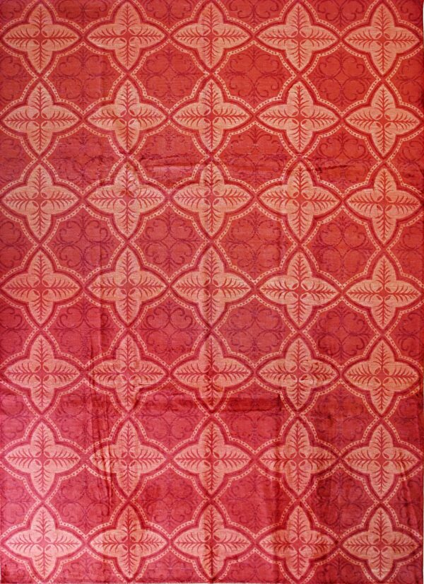 A plush crimson rug features a repeating trellis pattern of light pink stylized floral quatrefoils.