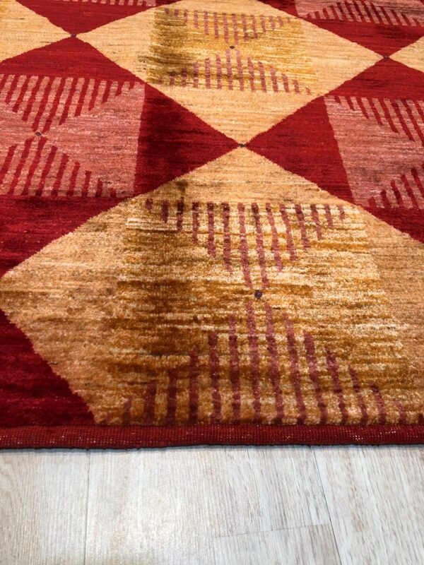 Close-up of a medium-pile rug featuring large red and gold geometric patterns on light wood flooring.