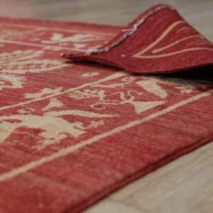 A close-up of a red and beige patterned flatweave rug curled on light wood floor.