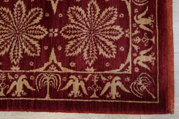 Burgundy textured rug with a tan repeating floral and stylized bird pattern on light wood flooring.