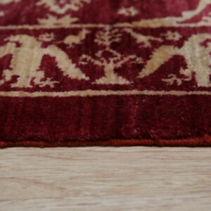 The red rug edge shows a stylized cream bird and floral pattern on light wooden flooring.