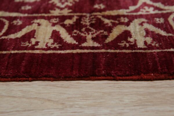 The red rug edge shows a stylized cream bird and floral pattern on light wooden flooring.