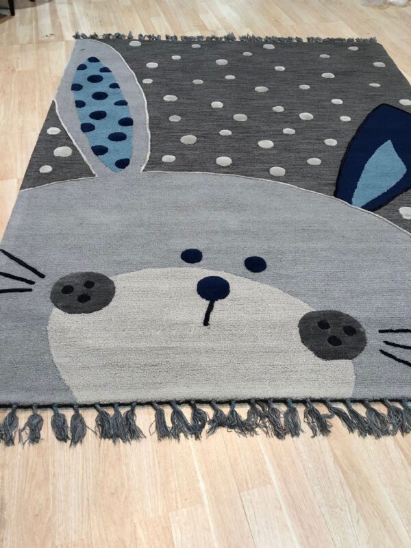 Grey rabbit patterned rug featuring blue ears, dark polka dots, and textured pile on light wood flooring.