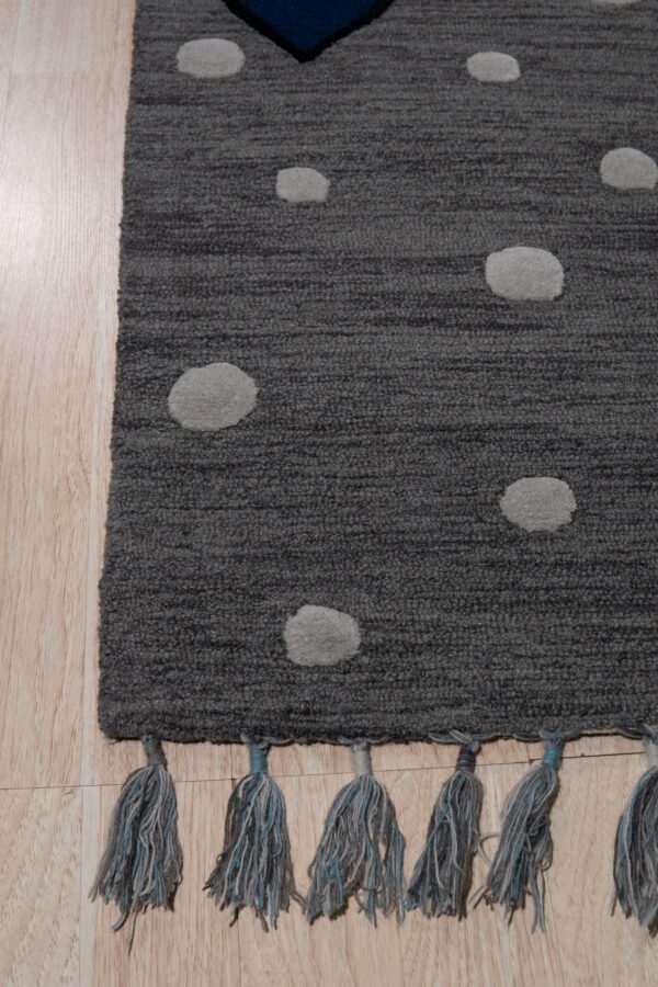 Dark gray textured rug with light gray dots and blue tassels rests on light hardwood planks.