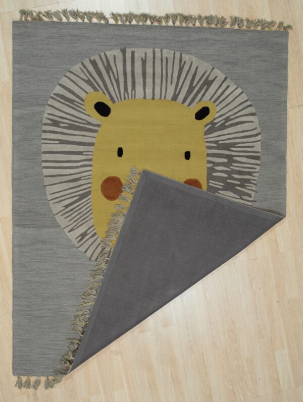 A gray rug featuring a yellow lion face pattern is partially folded back on pale wood floors.