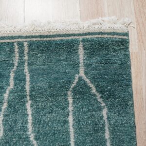 Shaggy teal rug with thick, uneven off-white lines and fringe on light wood flooring.