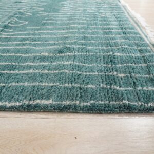 Thick-pile turquoise rug with horizontal cream stripes and fringe sits on light wood flooring.