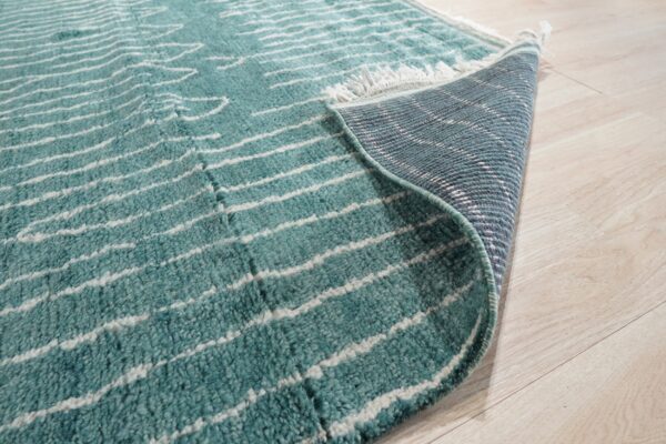 Teal and white striped high-pile rug partially rolled back on light blonde wood flooring.