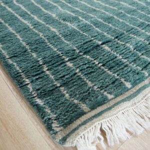 Textured teal rug featuring a white lattice pattern and thick fringe resting on light wood planks.