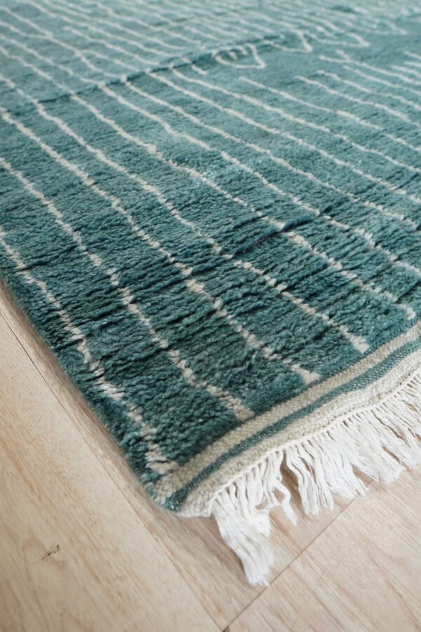 Textured teal rug featuring a white lattice pattern and thick fringe resting on light wood planks.
