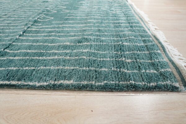 Textured teal and white striped high-pile rug featuring fringe and lying on a pale wooden floor.