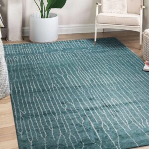 A teal rug with irregular white stripes covers light wood flooring beside a white chair.