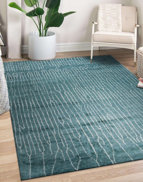 A teal rug with irregular white stripes covers light wood flooring beside a white chair.