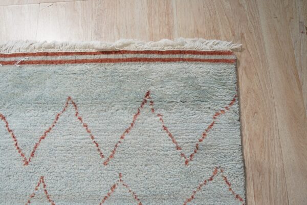 Pale blue shag rug with reddish-orange zigzag patterns and fringe rests on light wood flooring.