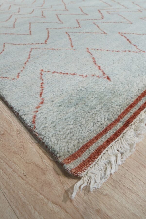 Shaggy off-white rug with a rust geometric pattern, striped border, and fringe on wood floor.