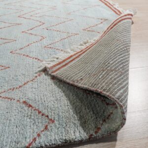 Textured blue rug with red zigzag lines, showing the striped woven backing on light wood floor.