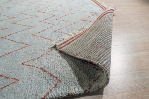 Textured blue rug with red zigzag lines, showing the striped woven backing on light wood floor.