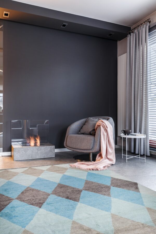 Blue and brown geometric diamond rug anchors a modern room with a gray chair and fireplace.