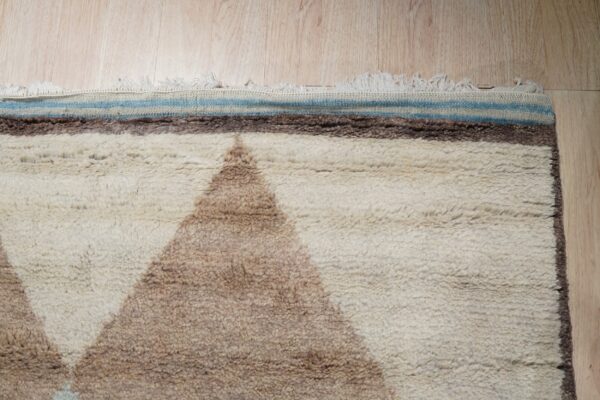 Shaggy cream and brown geometric rug edge featuring blue stripes and white fringe on a wood floor.