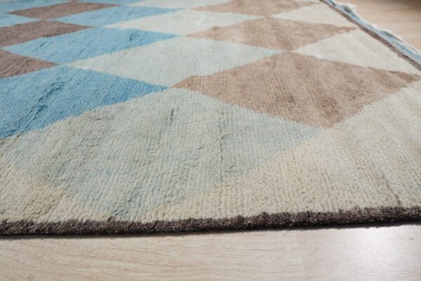Close view of a high-pile rug with blue, tan, and cream diamond patterns on light wood flooring.