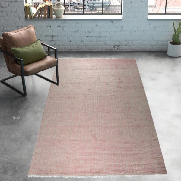 Muted pink low-pile rug on gray concrete flooring next to a leather armchair and white exposed brick wall.
