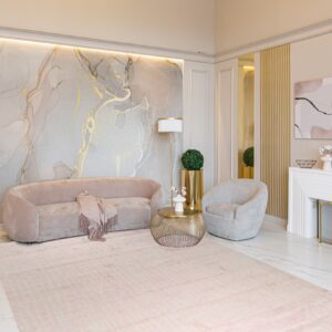 Pale pink striped area rug placed under a curved velvet sofa in a glamorous room with marble floors.