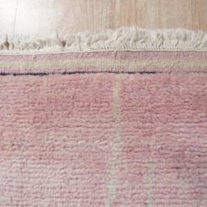 High-pile pink rug with white vertical stripes and cream fringe lying on light wood flooring.