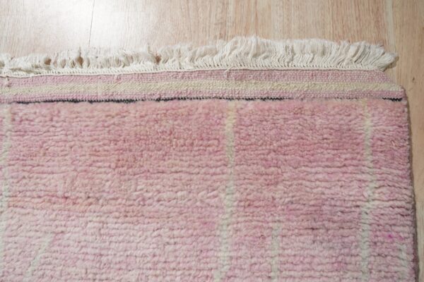 High-pile pink rug with white vertical stripes and cream fringe lying on light wood flooring.