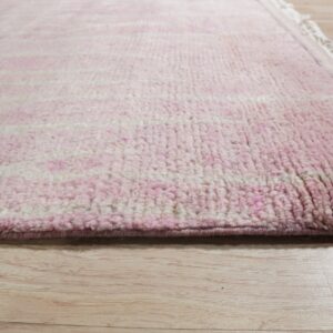 Close up of a thick pink and cream striped rug with fringe on light wood flooring.