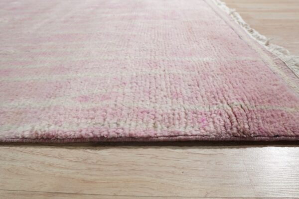 Close up of a thick pink and cream striped rug with fringe on light wood flooring.