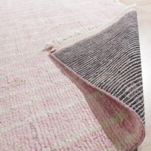 Pink high-pile rug showing horizontal stripes and a black and pink woven backing on light wood flooring.