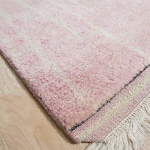 Pink high-pile rug with faint white stripes and long fringe rests on light-colored wood flooring.