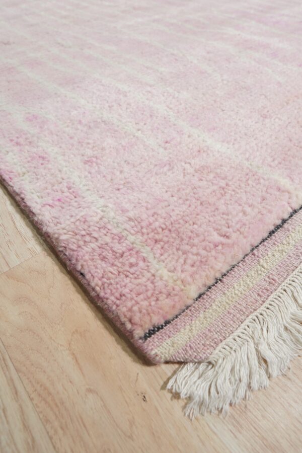 Pink high-pile rug with faint white stripes and long fringe rests on light-colored wood flooring.