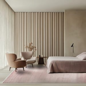 Light pink rug covers a light wood floor in a bedroom with beige ribbed walls and velvet chairs.