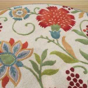 Round, textured ivory rug featuring vibrant floral designs in orange, teal, green, and maroon on a wood floor.