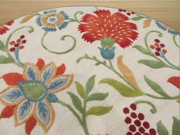 Round, textured ivory rug featuring vibrant floral designs in orange, teal, green, and maroon on a wood floor.