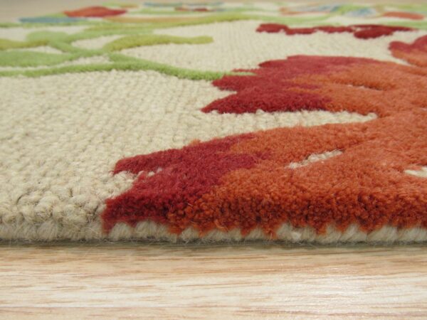 Side profile close-up of a textured rug with red, orange, and green floral designs on light wood floor.